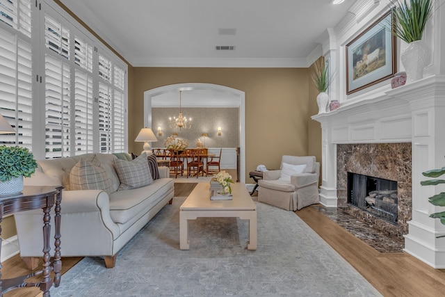 living room with a premium fireplace, ornamental molding, wood-type flooring, and an inviting chandelier