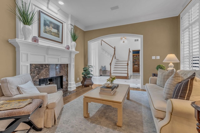 living room with a high end fireplace, ornamental molding, and light wood-type flooring