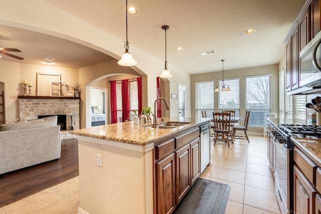 kitchen with light tile patterned flooring, sink, hanging light fixtures, an island with sink, and stainless steel appliances