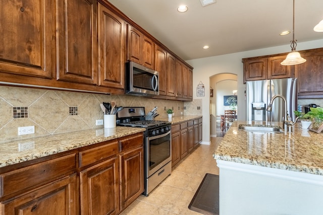 kitchen featuring sink, tasteful backsplash, decorative light fixtures, appliances with stainless steel finishes, and light stone countertops