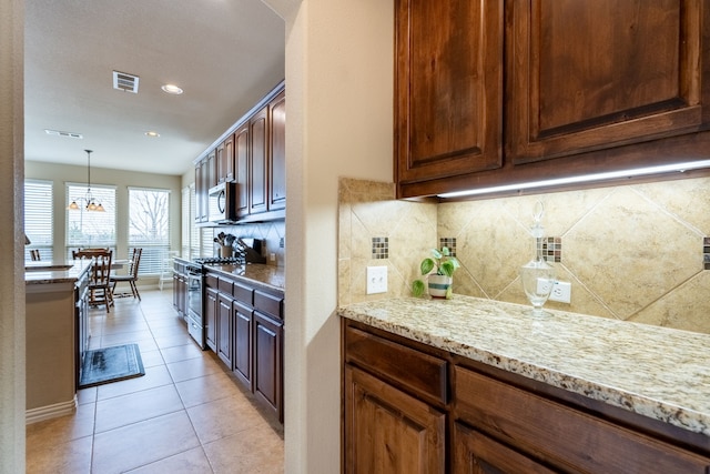 kitchen with light tile patterned flooring, tasteful backsplash, decorative light fixtures, stainless steel appliances, and light stone countertops