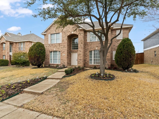 traditional-style home featuring brick siding, a front lawn, and fence