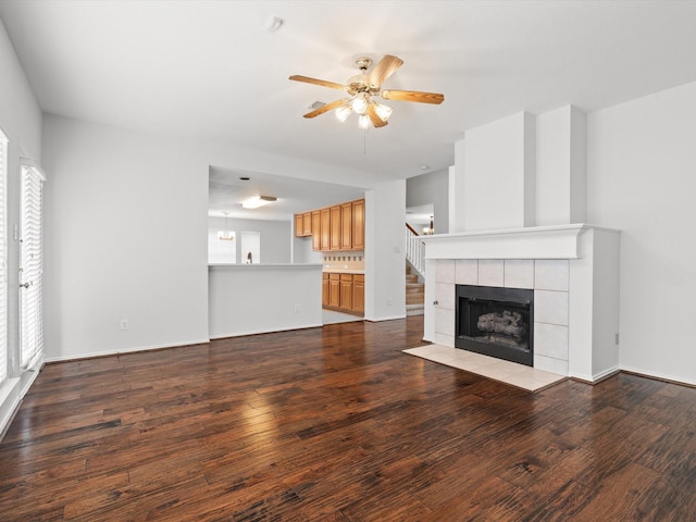 unfurnished living room with a tiled fireplace, ceiling fan, a wealth of natural light, and light wood-type flooring