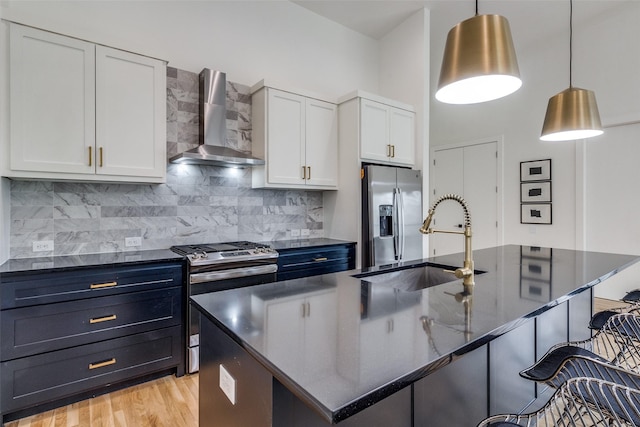 kitchen with wall chimney range hood, an island with sink, appliances with stainless steel finishes, and white cabinets