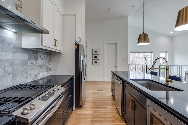 kitchen with stainless steel appliances, a sink, white cabinets, wall chimney exhaust hood, and dark countertops