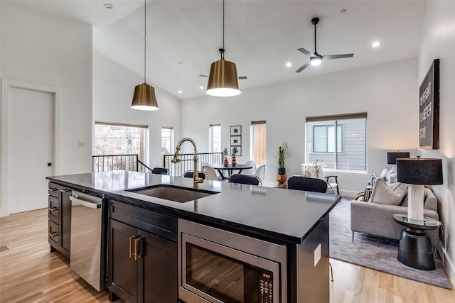 kitchen with appliances with stainless steel finishes, dark countertops, a center island with sink, and a sink