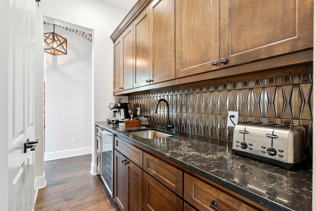 bar featuring wine cooler, sink, hanging light fixtures, dark stone countertops, and dark hardwood / wood-style flooring