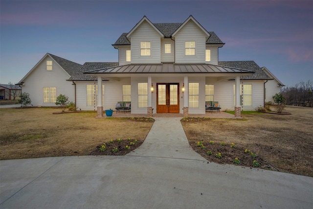 view of front facade featuring metal roof, a porch, french doors, roof with shingles, and a standing seam roof