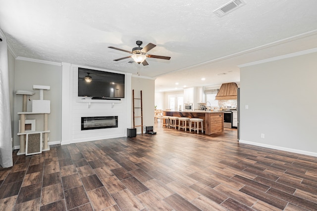 living room featuring dark wood-type flooring, ornamental molding, a fireplace, and a textured ceiling