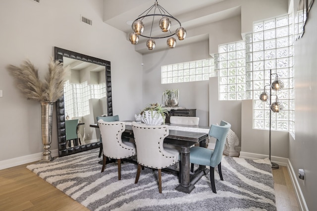 dining room with a notable chandelier, visible vents, baseboards, and wood finished floors