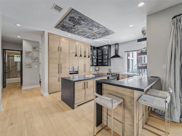 kitchen featuring visible vents, dark countertops, a breakfast bar, and wall chimney exhaust hood