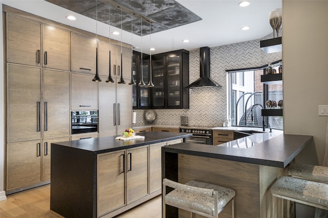 kitchen featuring black oven, a sink, a kitchen bar, dark countertops, and wall chimney range hood