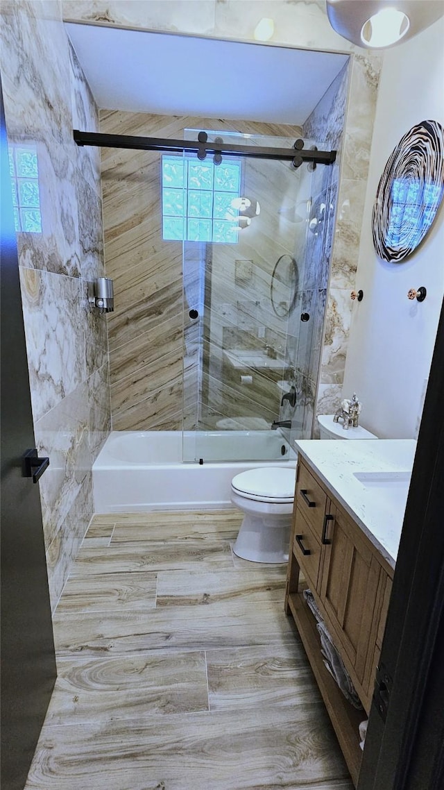 full bath featuring combined bath / shower with glass door, toilet, wood finished floors, and vanity