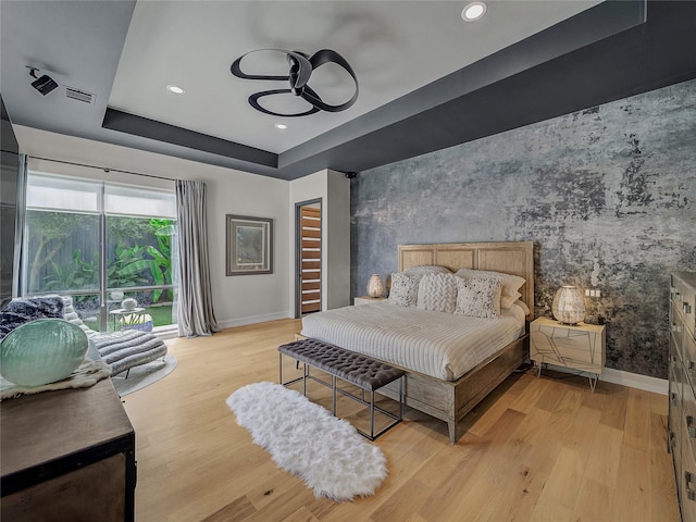 bedroom with wallpapered walls, an accent wall, baseboards, a tray ceiling, and light wood-style floors