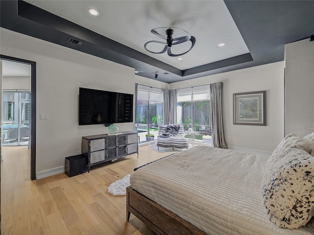 bedroom with visible vents, light wood-style flooring, a tray ceiling, baseboards, and access to exterior