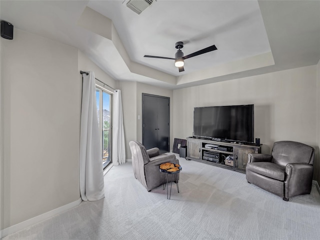 carpeted living room with visible vents, baseboards, a tray ceiling, and a ceiling fan