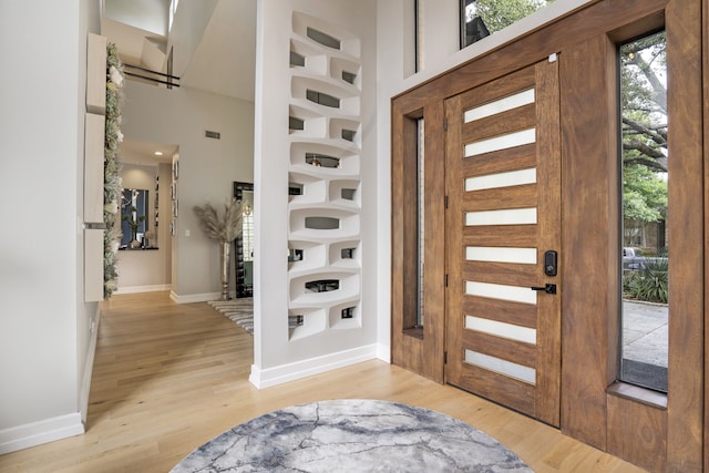 foyer with visible vents, baseboards, light wood-style floors, and a high ceiling