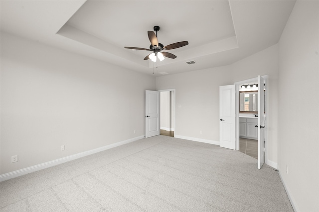 unfurnished bedroom with ensuite bathroom, a raised ceiling, baseboards, carpet flooring, and visible vents
