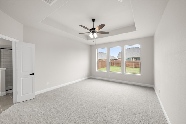 spare room with a raised ceiling, ceiling fan, baseboards, and light carpet