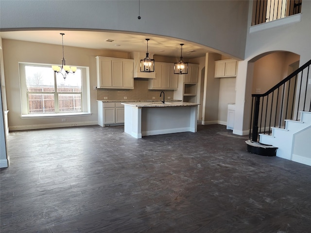 kitchen with a center island with sink, baseboards, dark wood finished floors, arched walkways, and decorative backsplash