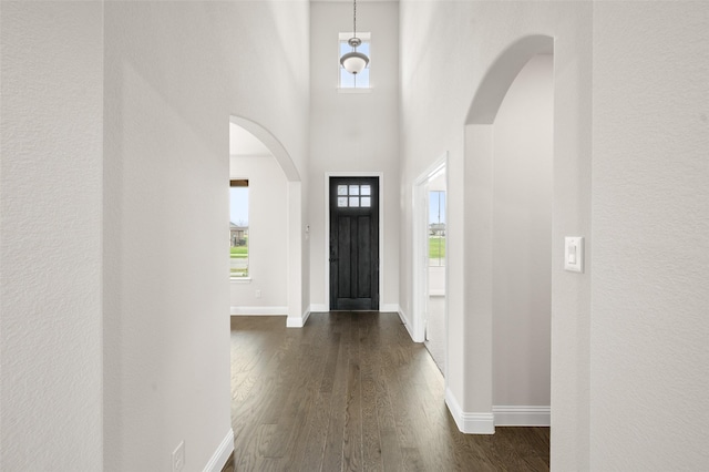 entrance foyer with arched walkways, dark wood-style flooring, and baseboards