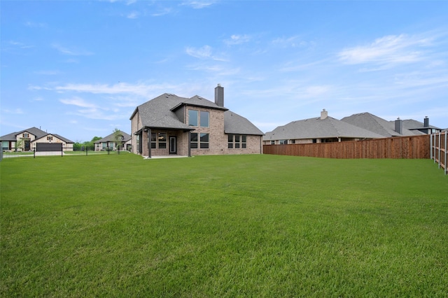 back of house featuring a chimney, a yard, brick siding, and a fenced backyard