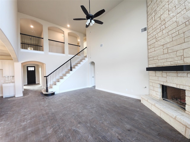 unfurnished living room with visible vents, baseboards, stairway, a stone fireplace, and wood finished floors