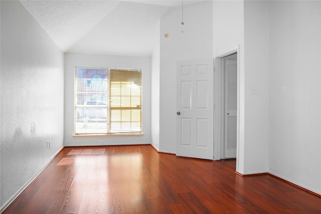 empty room with vaulted ceiling, a textured ceiling, and dark hardwood / wood-style flooring