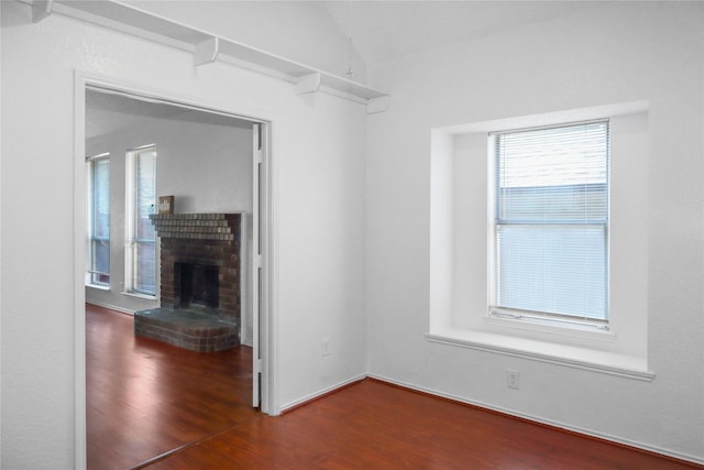 unfurnished living room with vaulted ceiling, a brick fireplace, and dark wood-type flooring