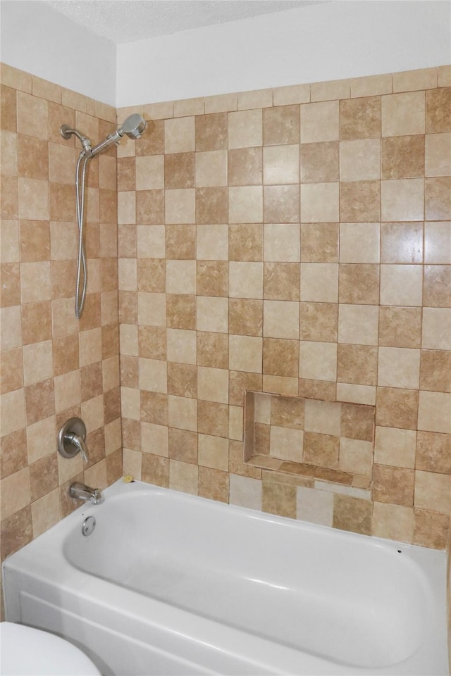 bathroom with toilet, tiled shower / bath combo, and a textured ceiling