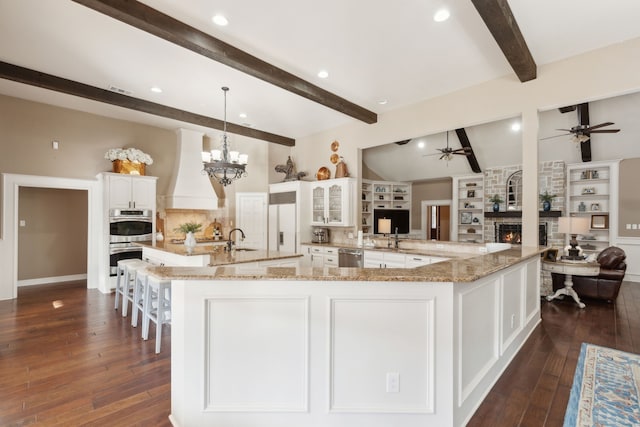 kitchen with white cabinetry, a large island with sink, appliances with stainless steel finishes, custom range hood, and light stone countertops