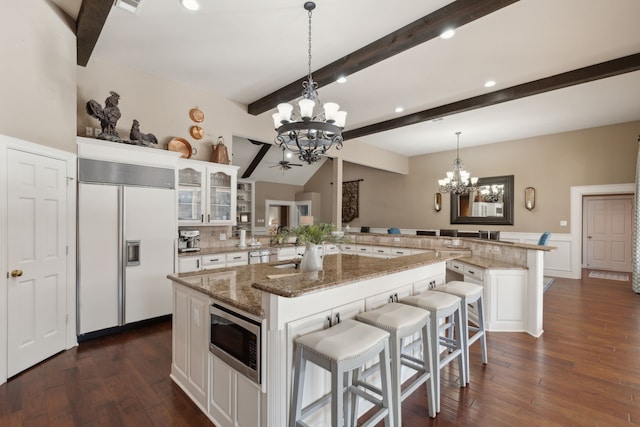 kitchen featuring a center island, built in appliances, white cabinets, a kitchen bar, and kitchen peninsula