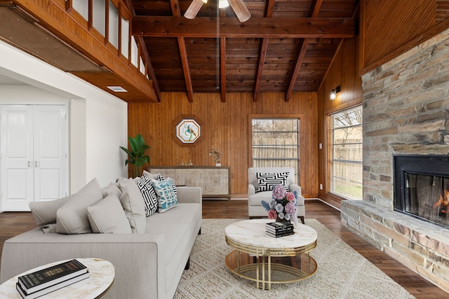 living room with beamed ceiling, wood-type flooring, a stone fireplace, and wood walls