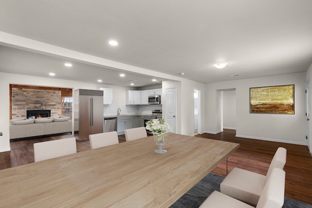 dining area with a stone fireplace, sink, and dark hardwood / wood-style floors