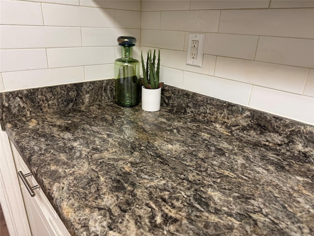 details featuring decorative backsplash, dark stone counters, and white cabinets