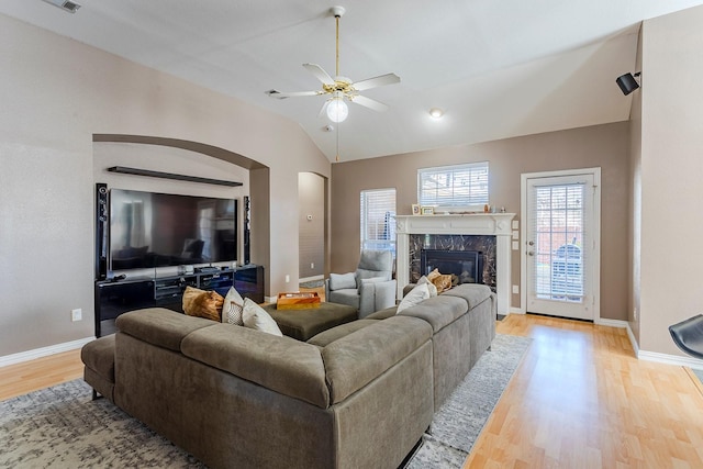 living room featuring a high end fireplace, vaulted ceiling, ceiling fan, and light wood-type flooring