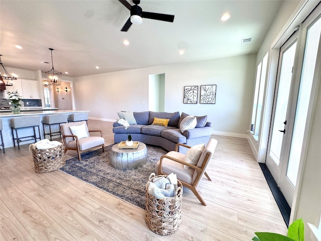 living room featuring ceiling fan with notable chandelier and light hardwood / wood-style flooring