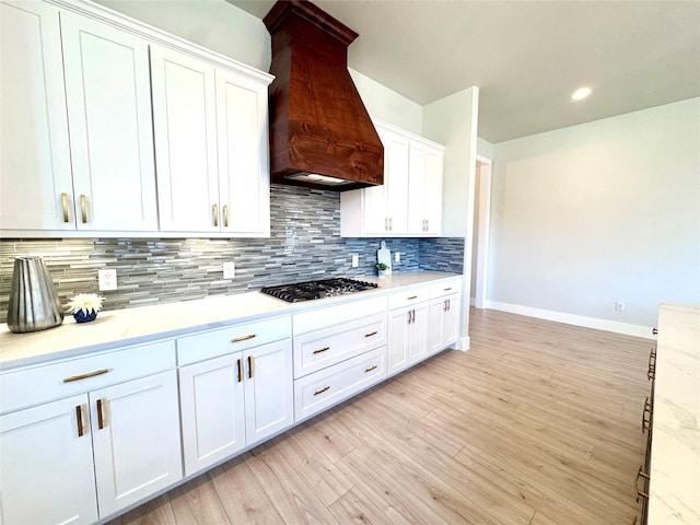 kitchen featuring light hardwood / wood-style flooring, custom range hood, white cabinets, stainless steel gas stovetop, and decorative backsplash