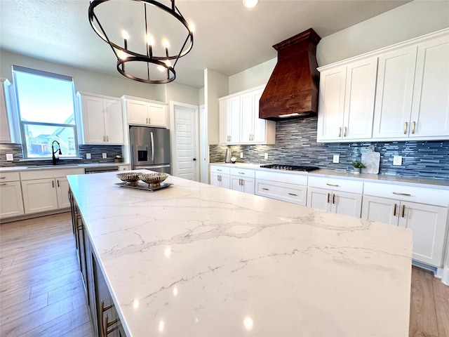 kitchen with white cabinets, premium range hood, stainless steel fridge, and decorative light fixtures