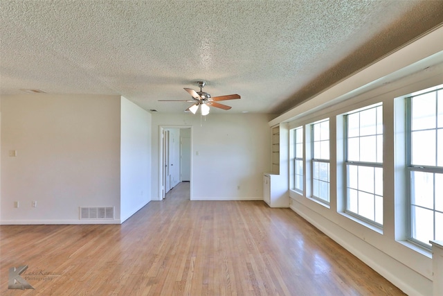 unfurnished room with ceiling fan, a healthy amount of sunlight, a textured ceiling, and light wood-type flooring