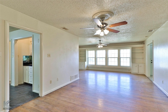 unfurnished room featuring ceiling fan, dark hardwood / wood-style floors, built in features, and a textured ceiling