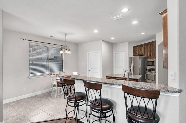 kitchen with a breakfast bar, appliances with stainless steel finishes, light stone countertops, decorative light fixtures, and kitchen peninsula