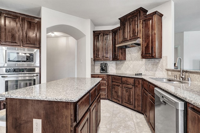 kitchen featuring appliances with stainless steel finishes, sink, a kitchen island, dark brown cabinets, and tasteful backsplash