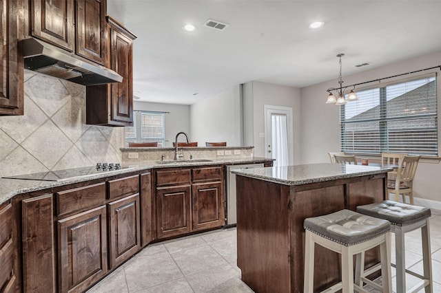 kitchen with sink, a breakfast bar, a center island, light stone counters, and stainless steel dishwasher