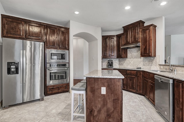 kitchen featuring sink, a center island, stainless steel appliances, light stone countertops, and tasteful backsplash