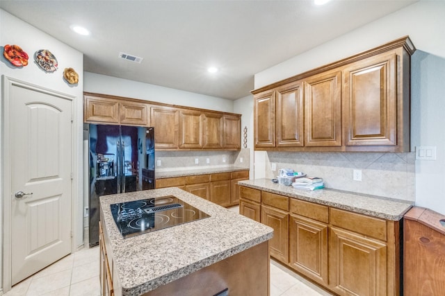 kitchen featuring light tile patterned floors, visible vents, a kitchen island, black appliances, and brown cabinets