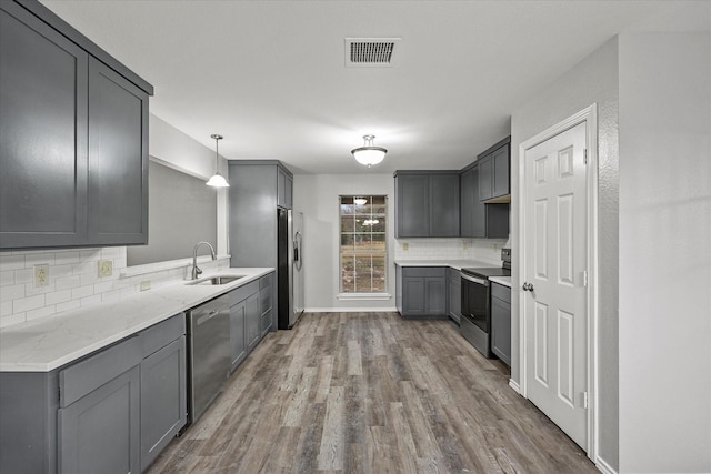 kitchen featuring gray cabinets, decorative light fixtures, wood-type flooring, sink, and stainless steel appliances