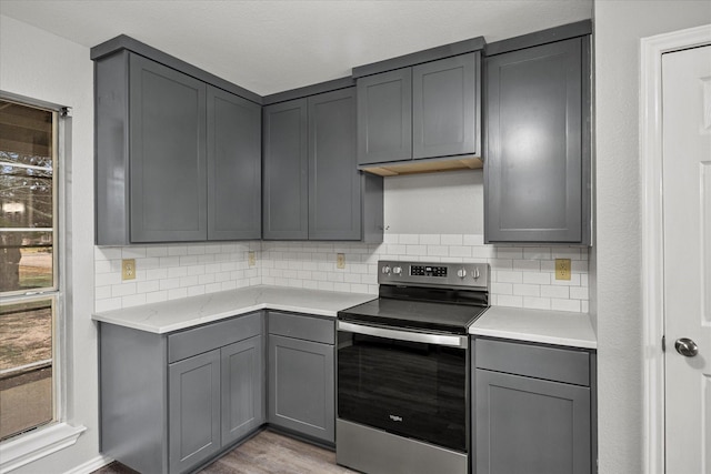 kitchen featuring stainless steel electric stove, light wood-type flooring, decorative backsplash, and gray cabinetry