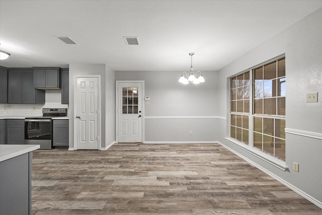 kitchen with decorative light fixtures, hardwood / wood-style flooring, gray cabinets, electric stove, and decorative backsplash