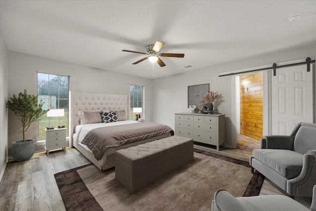 bedroom with hardwood / wood-style flooring, ceiling fan, and a barn door